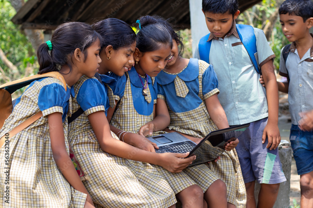 A group of children sitting on a bench, engrossed in a laptop screen, with curiosity and excitement.